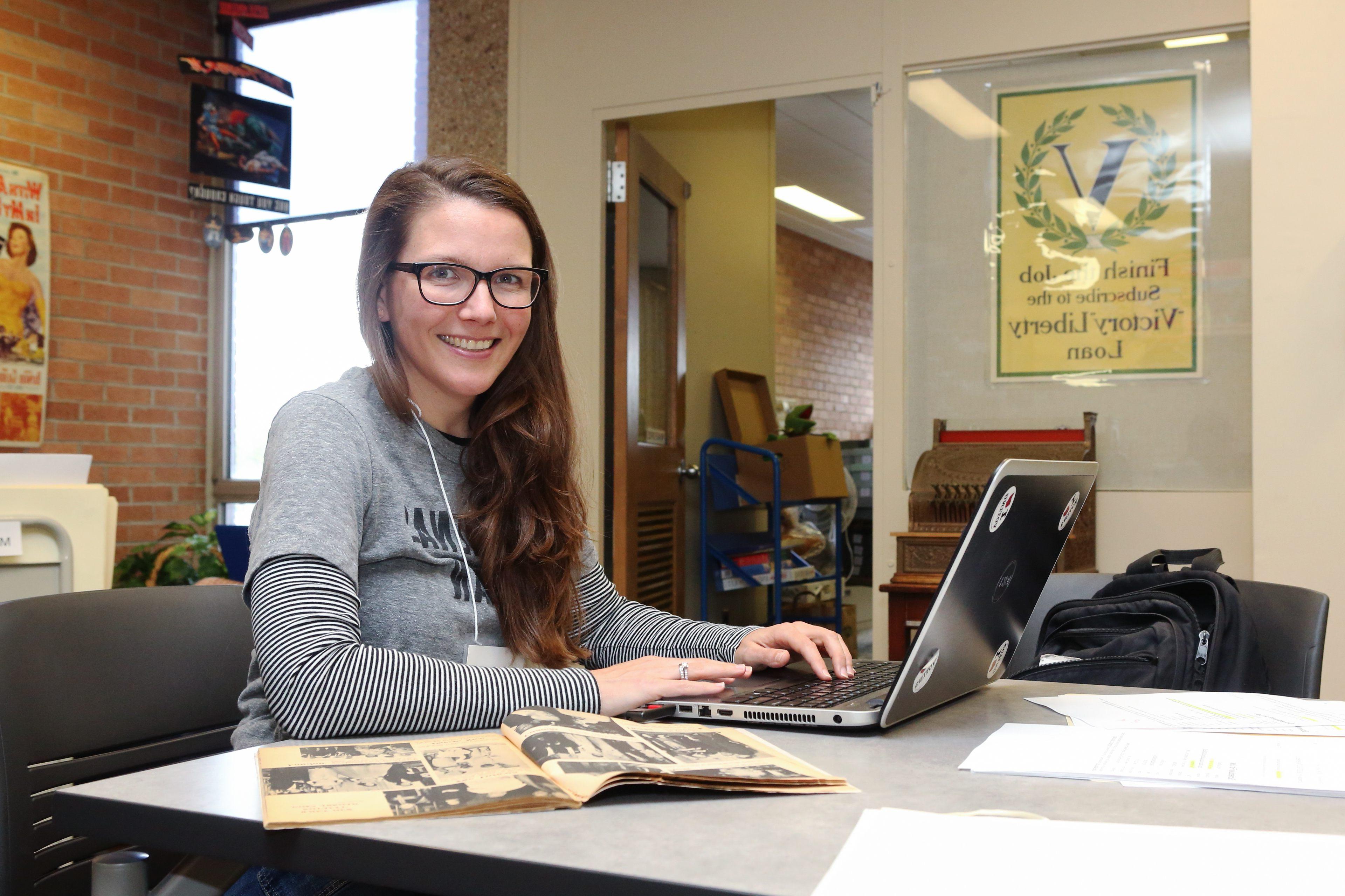 一位BGSU流行文化专业的女硕士生在电脑上工作，并在流行文化图书馆的大量馆藏中进行博天堂官方网站.